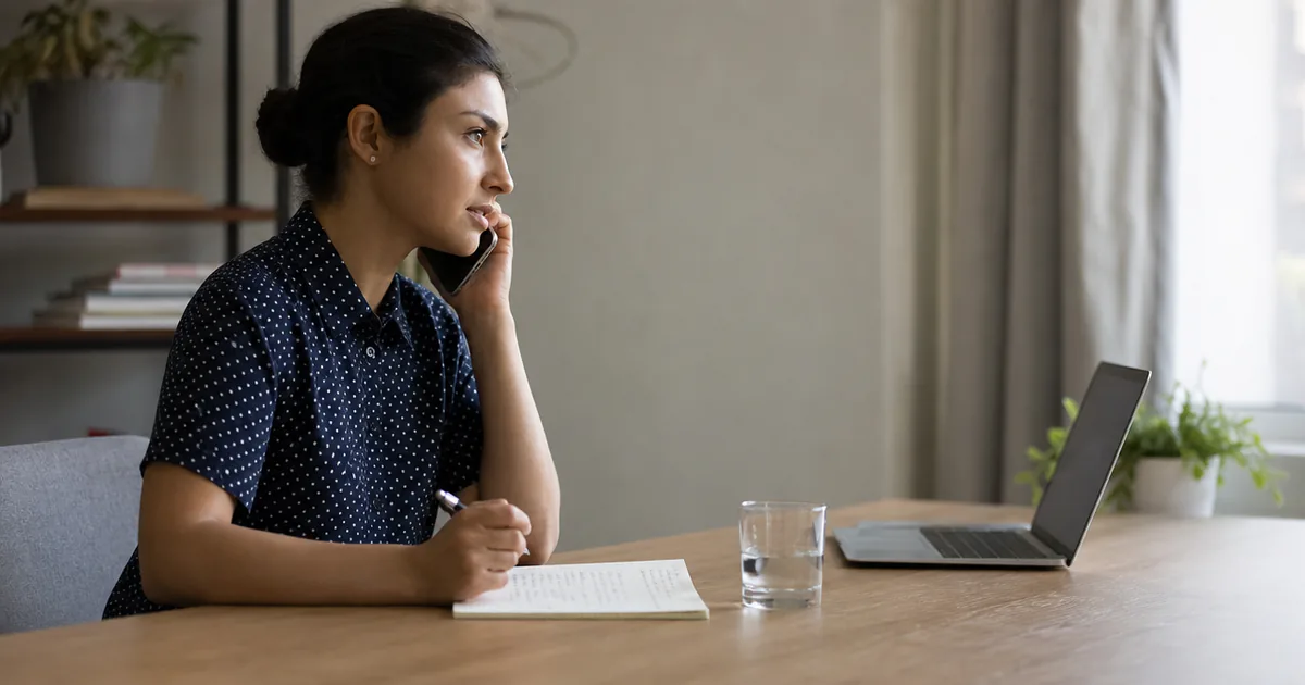 A candidate speaking on the phone beside a laptop and handwritten notes.